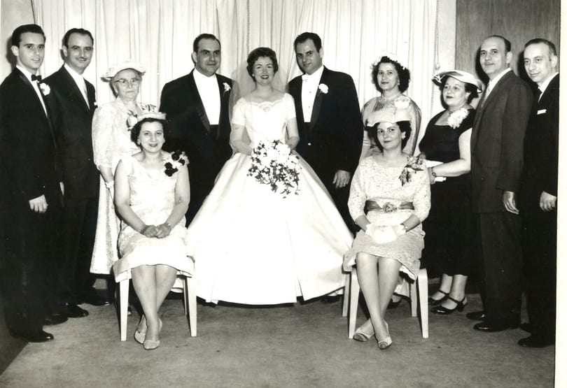 A black and white photo of a wedding party with the bride and groom surrounded by guests.