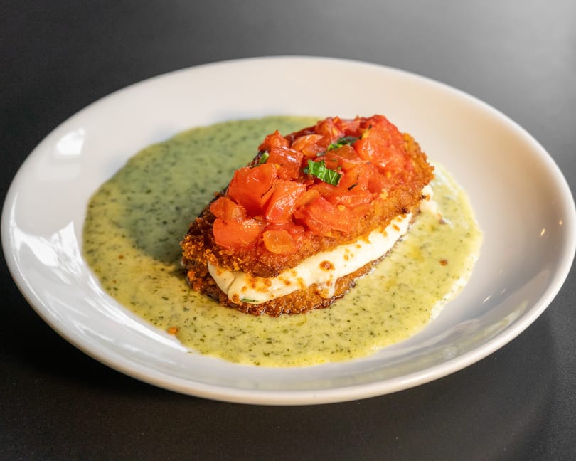 Crispy fried chicken topped with diced tomatoes and basil, served on a bed of green sauce.