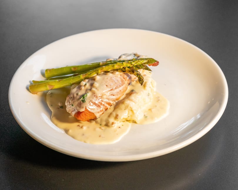 Pan-seared salmon with creamy sauce, mashed potatoes, and asparagus on a white plate.