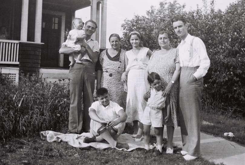 A black and white photo of a family of eight posing outdoors in front of a house.