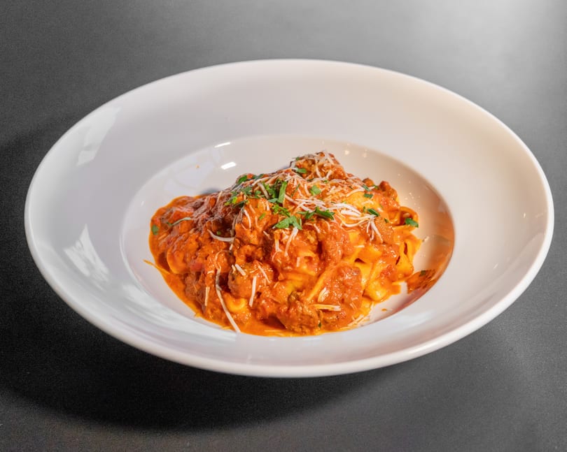 Pappardelle pasta with meatballs, red sauce, parmesan cheese, and parsley in a white bowl.