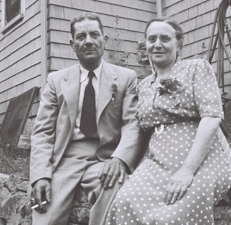 A black and white photo of a man and woman sitting outdoors, the man holding a cigarette.