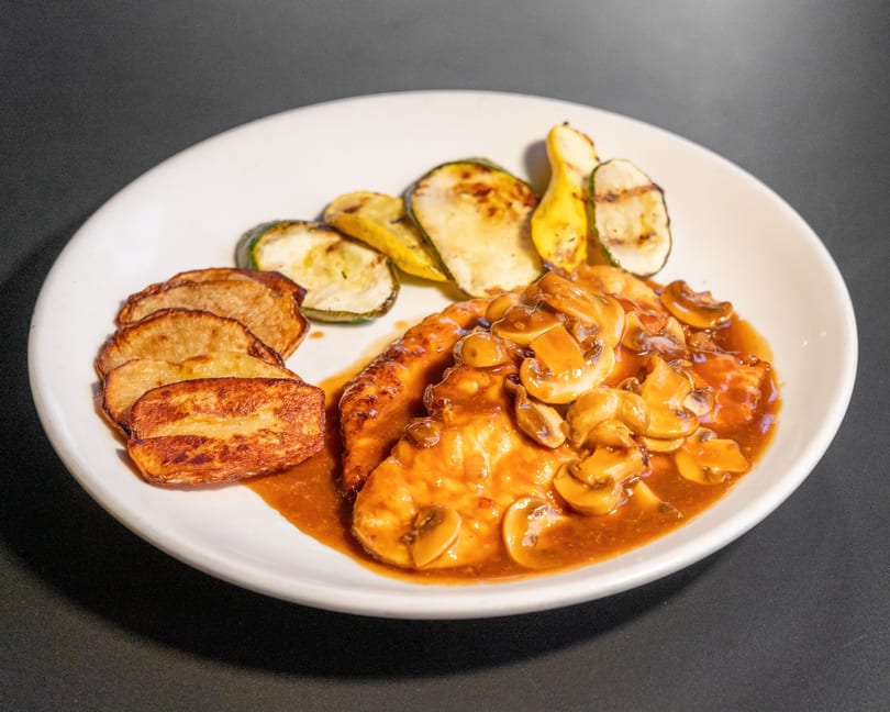 Chicken with mushroom sauce, roasted potatoes, and grilled zucchini on a white plate.