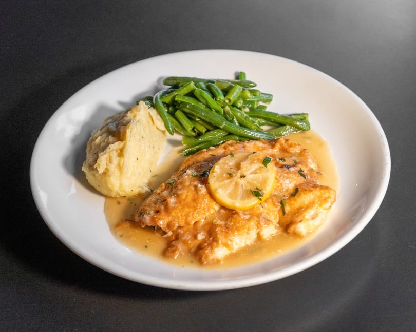 Lemon butter fish with mashed potatoes and green beans on a white plate.