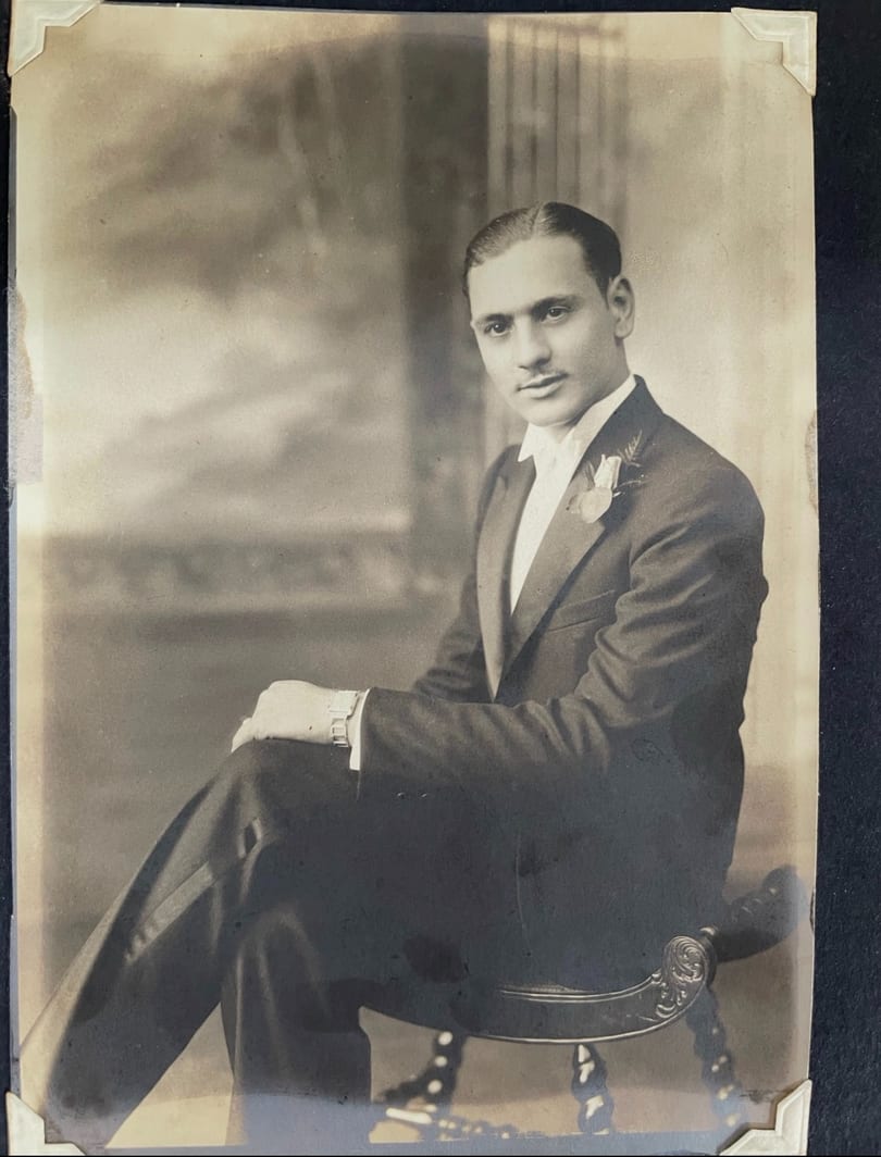 A vintage sepia portrait of a man in a tuxedo with a boutonnière, seated and looking at the camera.